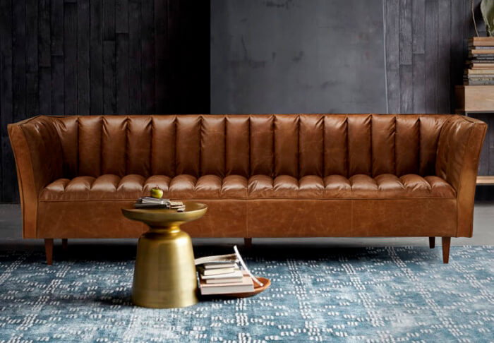 Brown panelled leather couch on grey-blue rug in living room with dark grey walls